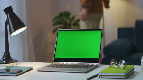 notebook-with-green-display-on-working-table-in-home-office-man-is-turning-off-table-and-floor-lamps-in-living-room-and-closing-cover-chroma-key-technology
